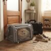 Small dog sitting inside a grey PetzVibes pet carrier by the front door, black carrier in the background