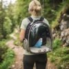 Woman hiking outdoors wearing the PetzVibes black Space Capsule Cat Backpack Carrier with a budgerigar inside.